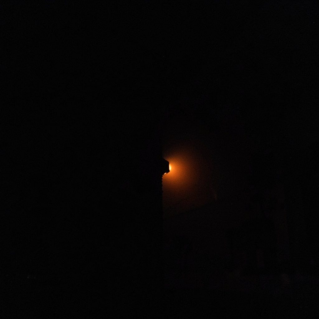 Dark, low-key photograph of a quiet agreement handshake at twilight, deep charcoal shadows, muted teal horizon, and a single coral-red glow in the distance.