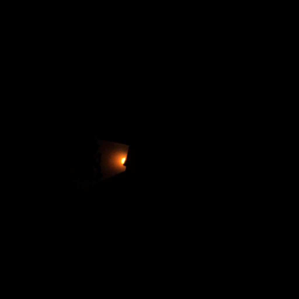 Dark, low-key photograph of a metallic anchor resting on a textured surface, deep charcoal shadows, and a single muted coral glow falling across the curved steel.