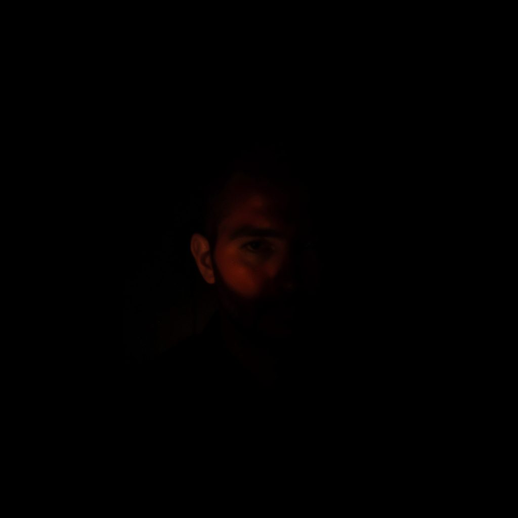 Moody, low-light photograph of a dark study scene, deep charcoal shadows, muted teal accents, and a single warm coral light glowing softly across a quiet desk.
